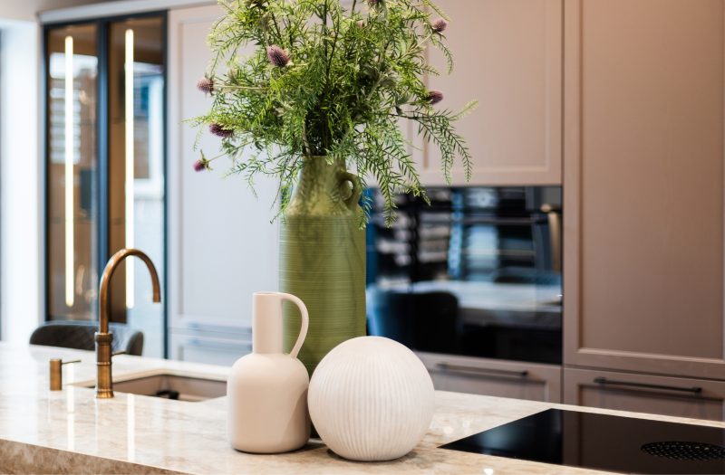 Nolte Lugano Lack kitchen display at the Amersham showroom featuring a stone island, integrated hob, brass tap and illuminated glass cabinetry.