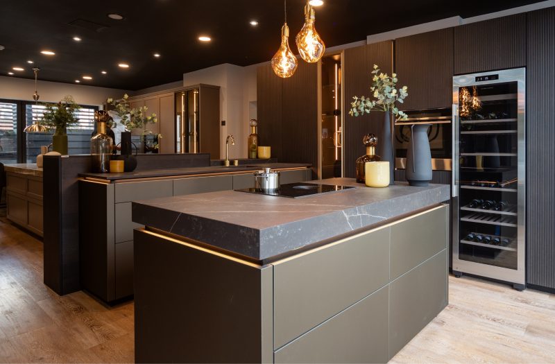 Nolte neoLodge kitchen display at the Amersham showroom with dark cabinetry, stone island worktop, integrated wine cooler and illuminated glass cabinets.