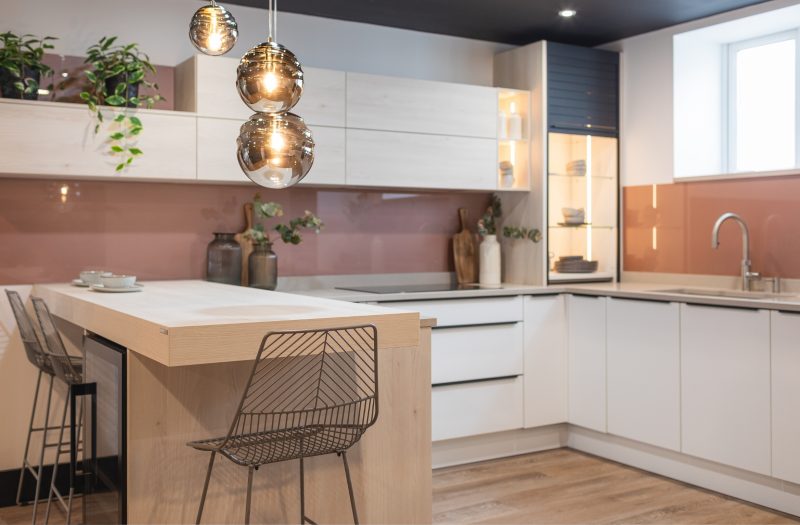 Nolte Soft Lack kitchen display in Amersham featuring light cabinetry, pink glass splashback, breakfast bar seating and illuminated display storage.