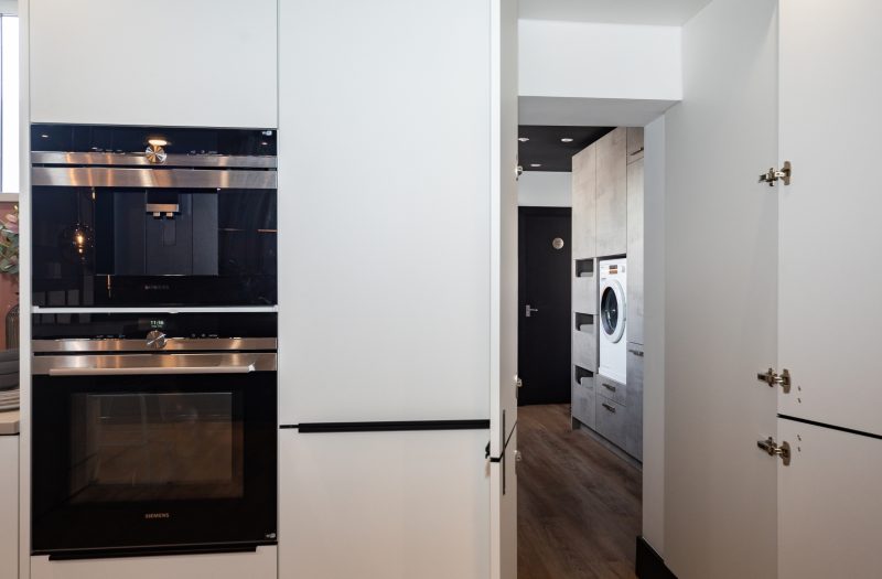 Nolte Soft Lack kitchen display at the Amersham showroom featuring a concealed doorway leading to a hidden utility room with integrated laundry appliances.