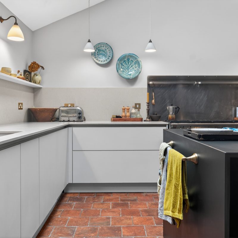 Brass rail with folded tea towels on a Plus Black island in a two-tone handleless kitchen, Nolte Amersham showroom project