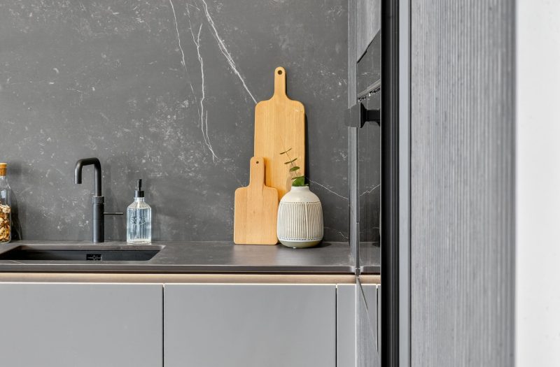 Close-up of the neoLodge kitchen display at Nolte Kitchens Bath featuring textured cabinetry, dark worktop and splashback, black sink and tap.