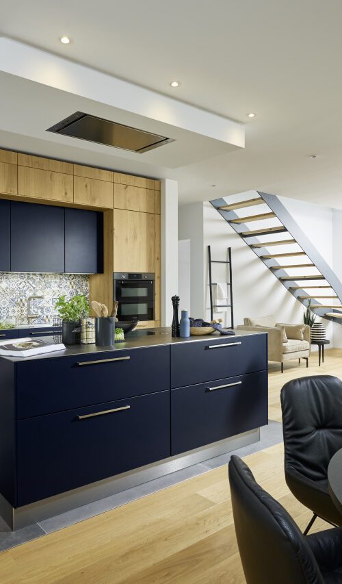 Alt Text: Nolte Soft Lack kitchen in deep navy blue matte lacquer with oak wood upper cabinets, central island and patterned tile splashback in open-plan living space