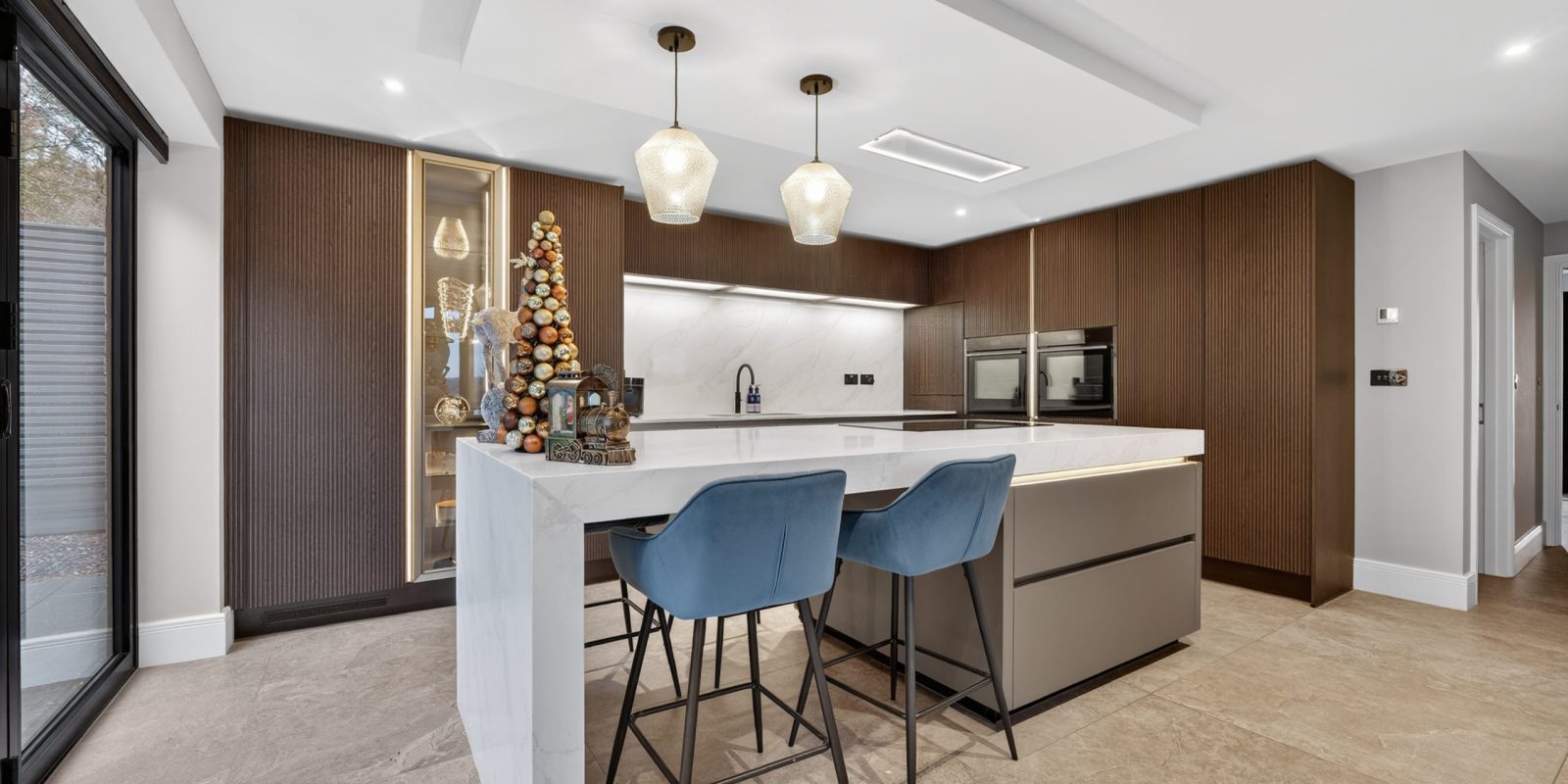 Lucy’s modern customer kitchen designed by Nolte Kitchens Amersham, featuring fluted neoLodge cabinetry in Blackened Oak, neoPure Gold doors and a large white waterfall kitchen island with seating.