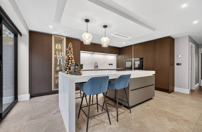 Lucy’s modern customer kitchen designed by Nolte Kitchens Amersham, featuring fluted neoLodge cabinetry in Blackened Oak, neoPure Gold doors and a large white waterfall kitchen island with seating.