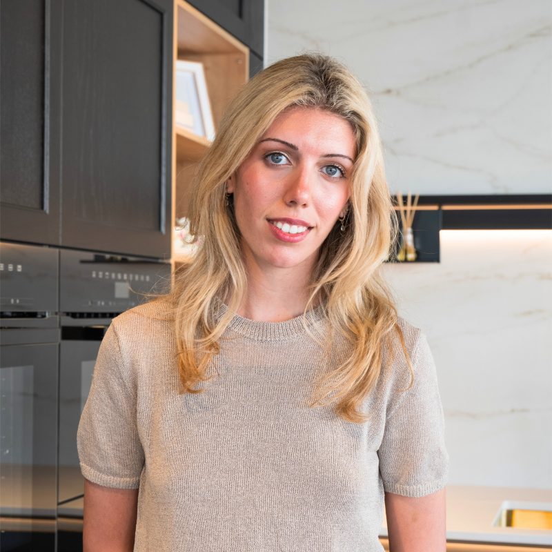 Kitchen designer, Vicky Sdrenia, at the Nolte Kitchens Cambridge showroom, standing in front of the Lugano Lack German kitchen display.