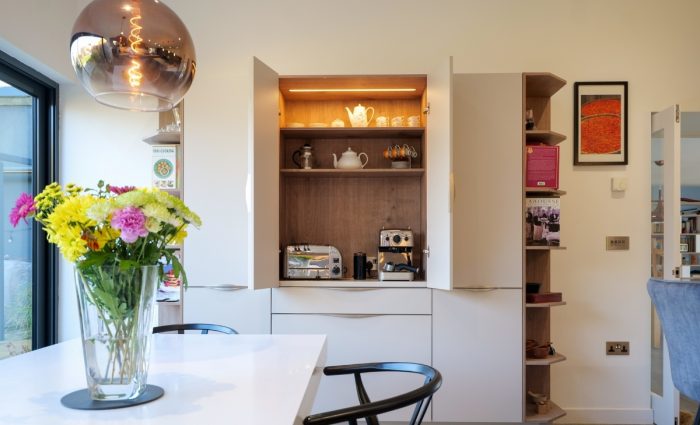 Bantry-style Nolte cabinetry opened to reveal a hidden coffee and breakfast station with integrated shelf lighting