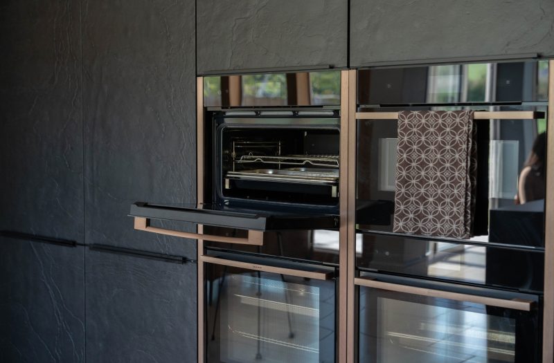 Detailed view of genuine stone veneer neoSLATE cabinetry in Rachel's dark kitchen in Henley-on-Thames. The textured black tall cabinets feature integrated NEFF ovens at eye level, combining natural slate finishes with contemporary German kitchen design.