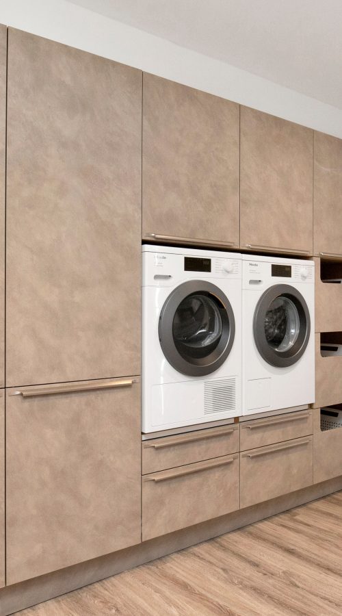 Nolte Lucca utility room in concrete effect matte fronts with integrated washing machine and tumble dryer, floor-to-ceiling cabinetry and open shelving
