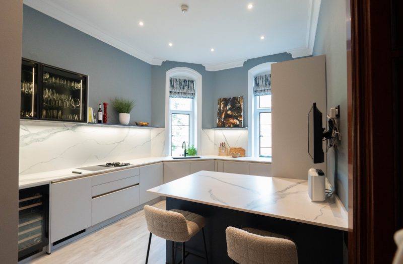 Platinum Grey U-shaped Nolte kitchen with a Blueberry peninsula, bouclé bar stools and illuminated glass wall cabinets