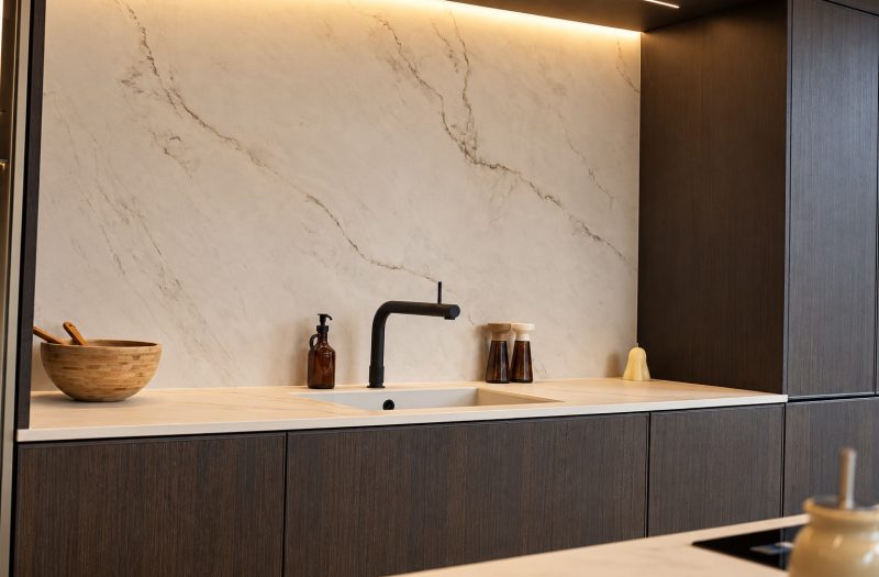 Dark wood kitchen with a full-height marble-effect splashback, under-cabinet lighting and black tap at the Nolte Wakefield showroom