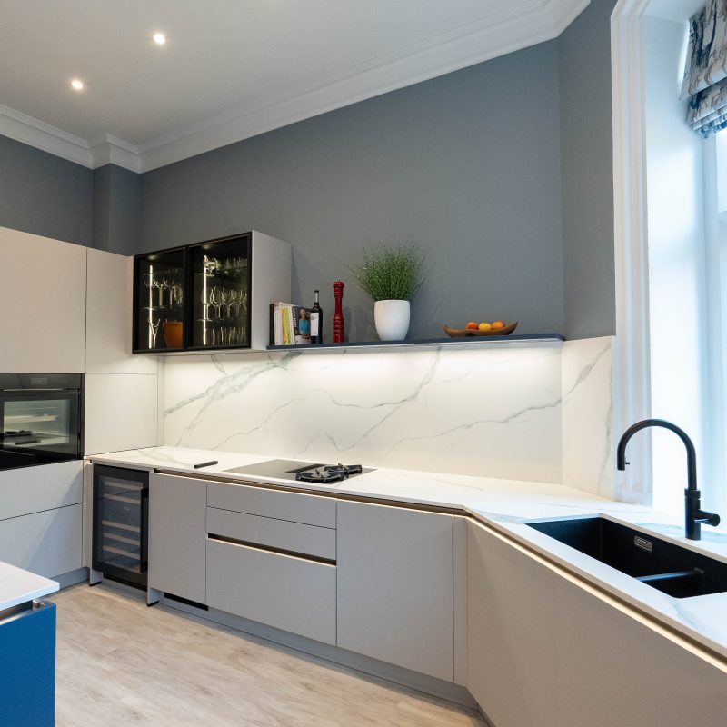 Platinum Grey handleless Nolte units with tall housing, built-in oven, wine cooler, black sink and Laminam marble-effect splashback